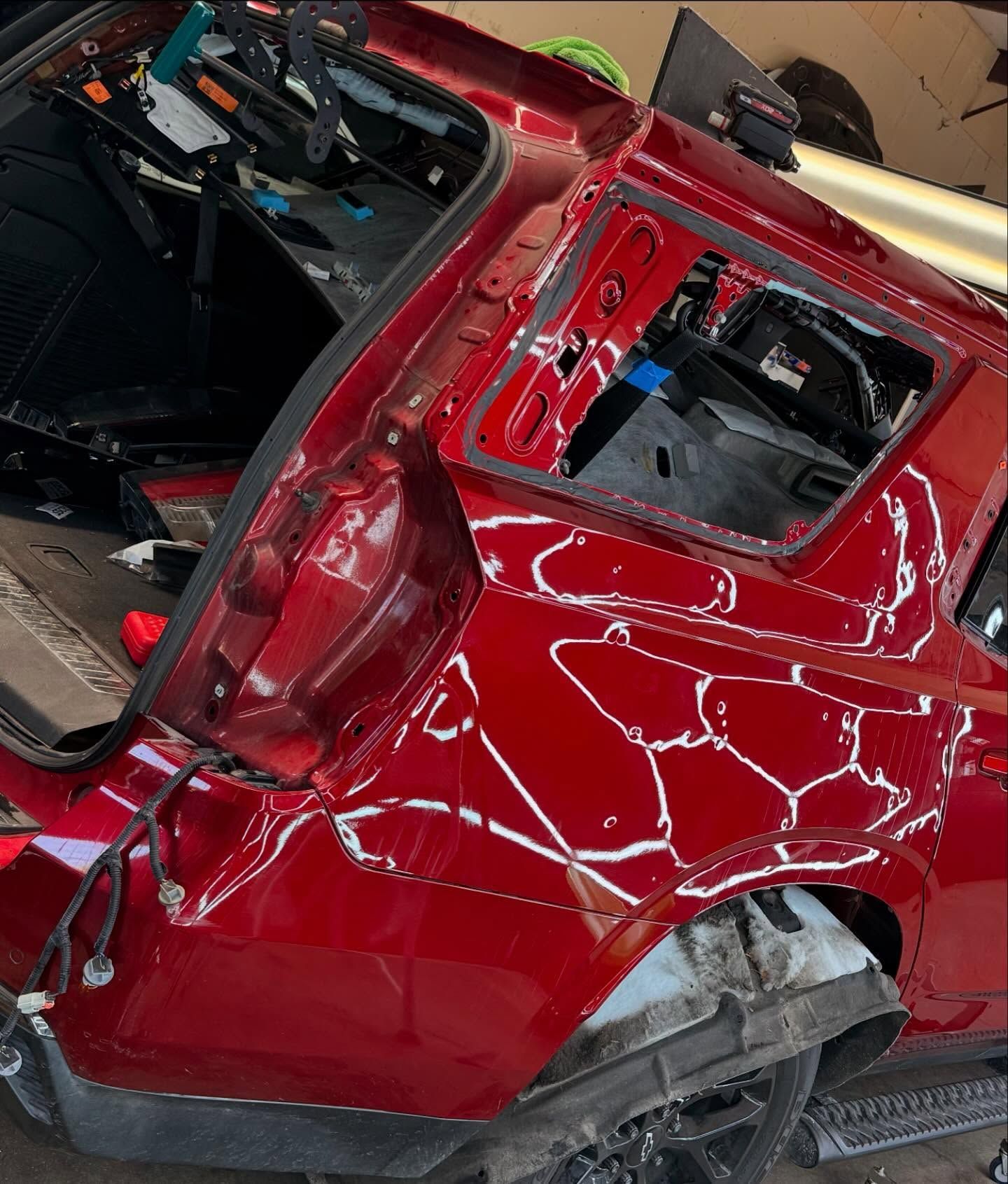 Red car with extensive rear damage in a repair shop, showing exposed internal structure.