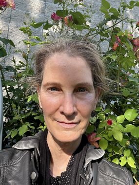 Kate Parkinson in a black jacket is standing in front of a bush of flowers.