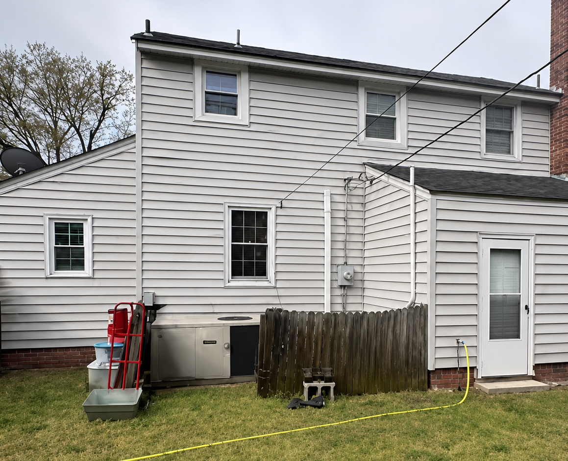 Back of a white two-story house with windows, a small porch, fence, and lawn