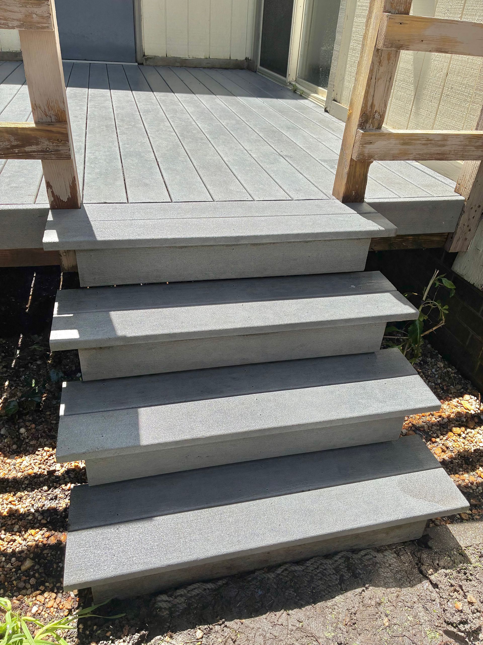 Concrete steps leading to a small porch with wooden railings and a door in the background.
