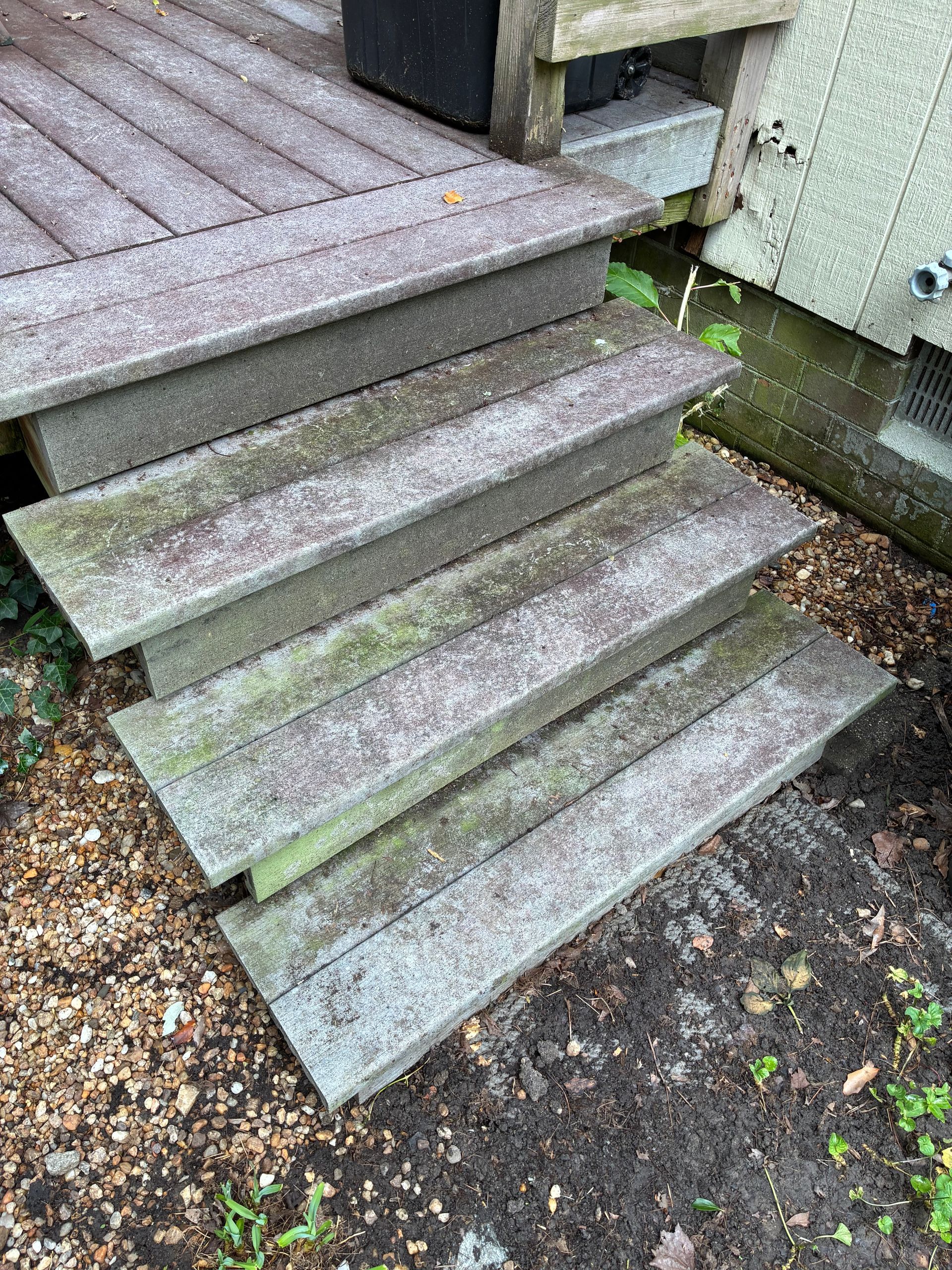 Weathered concrete steps leading to a raised deck, with moss and gravel beside them.