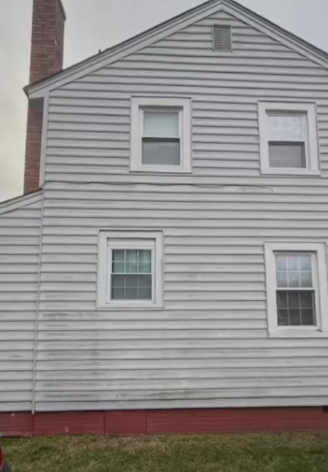 Side of a gray house with white trim, three windows, and a red foundation.