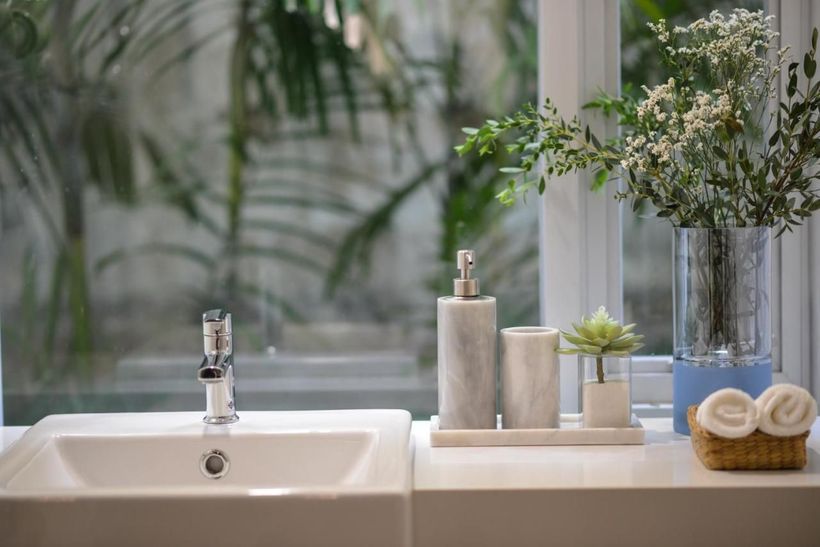 A bathroom sink with a vase of flowers on the counter next to a window.