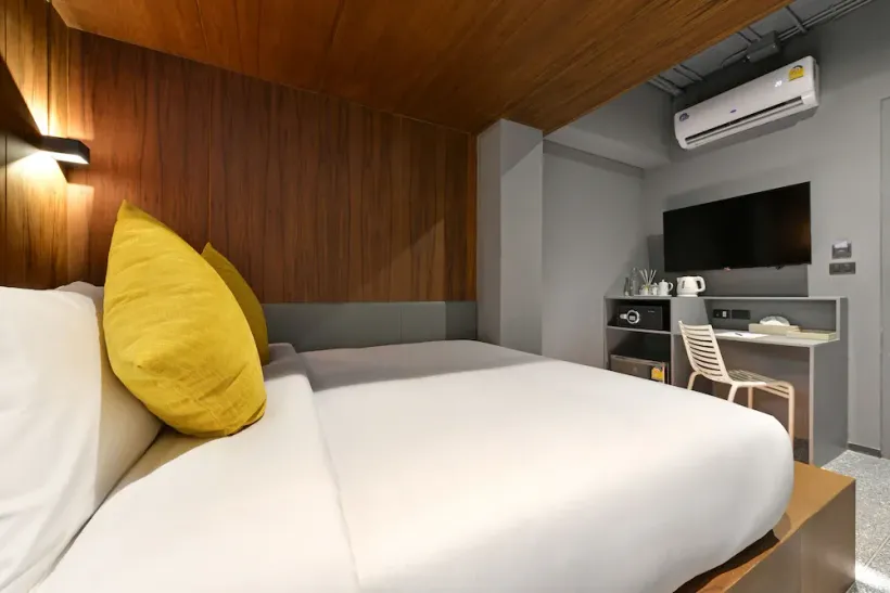A hotel room with a bed , desk , television and air conditioner.