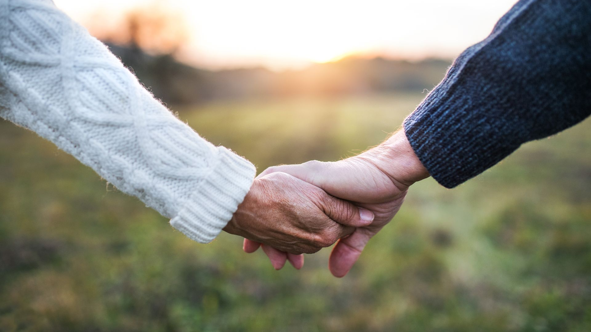 Two hands clasped together outdoors, one in a white sweater and one in a dark blue sleeve.