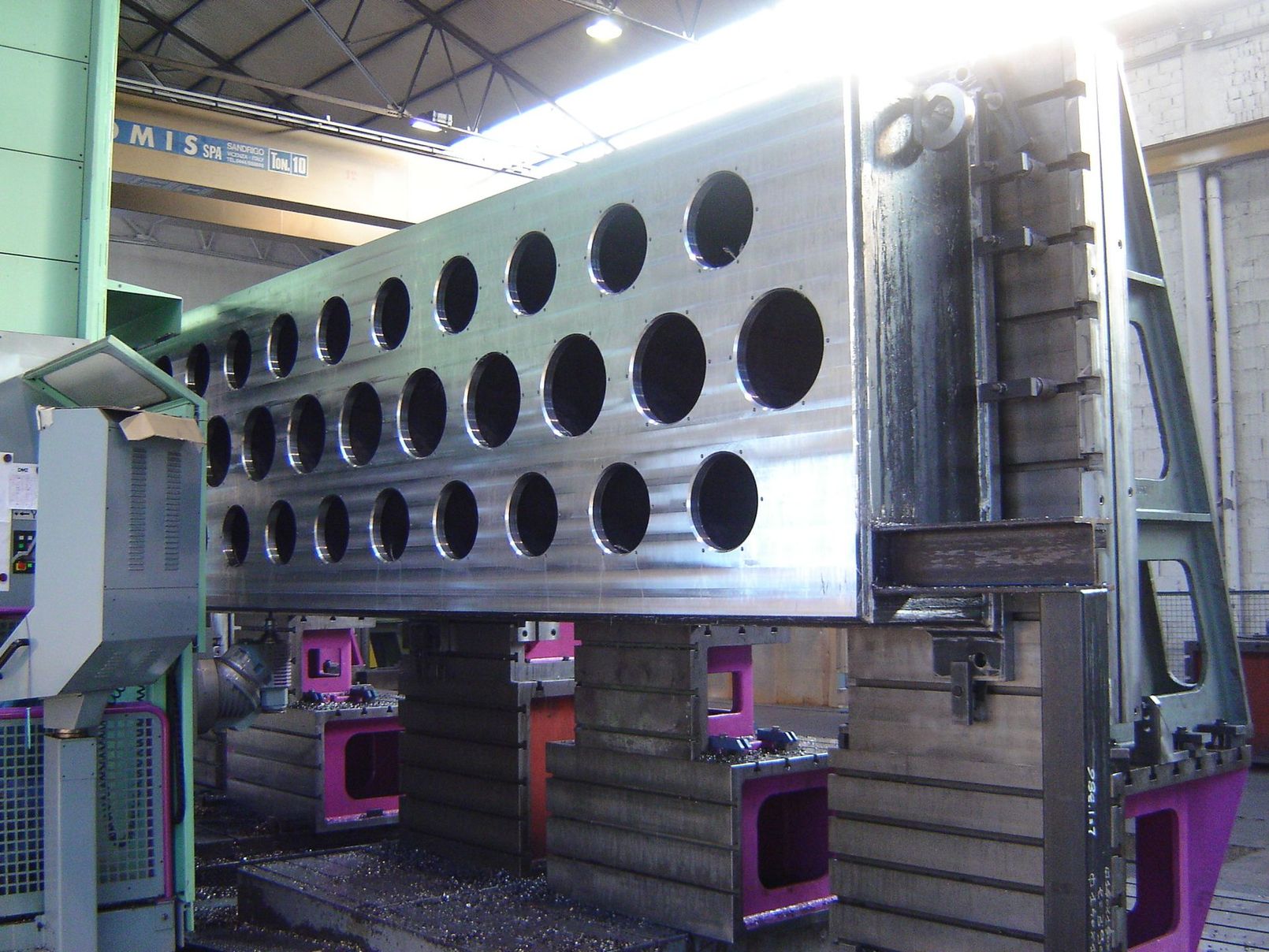 Una macchina utensile industriale sta lavorando un grande blocco di metallo grigio in un'officina di fabbrica.