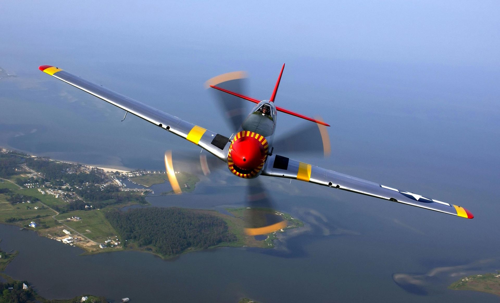 A red and yellow plane is flying over a body of water
