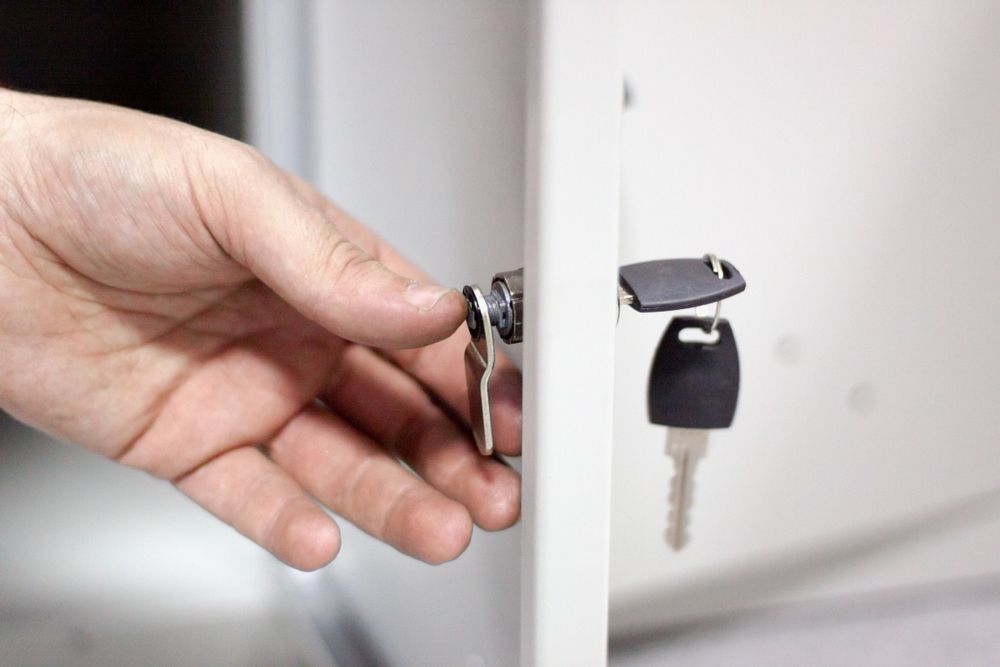 Hand Turning a Key in A White Cabinet Lock — CQR Locksmiths in Walgett, NSW