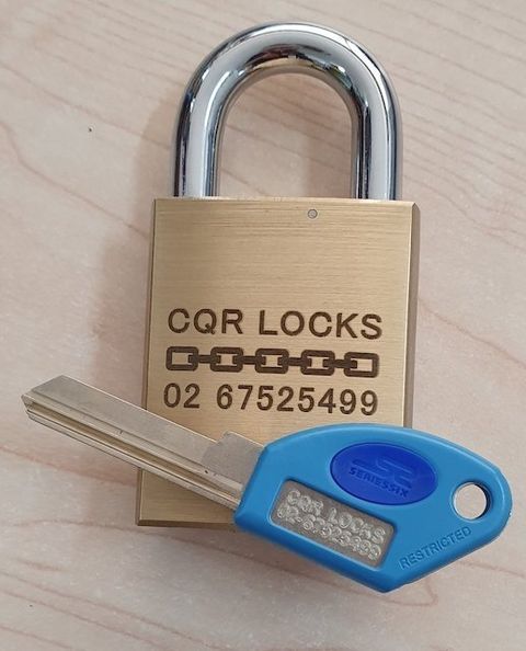 Brass CQR Lock With A Matching Blue Key Displaying Company Details On A Light Wooden Surface — CQR Locksmiths In Moree, NSW
