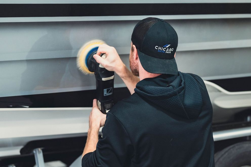 Person polishing a sleek gray vehicle with a power buffer in a garage
