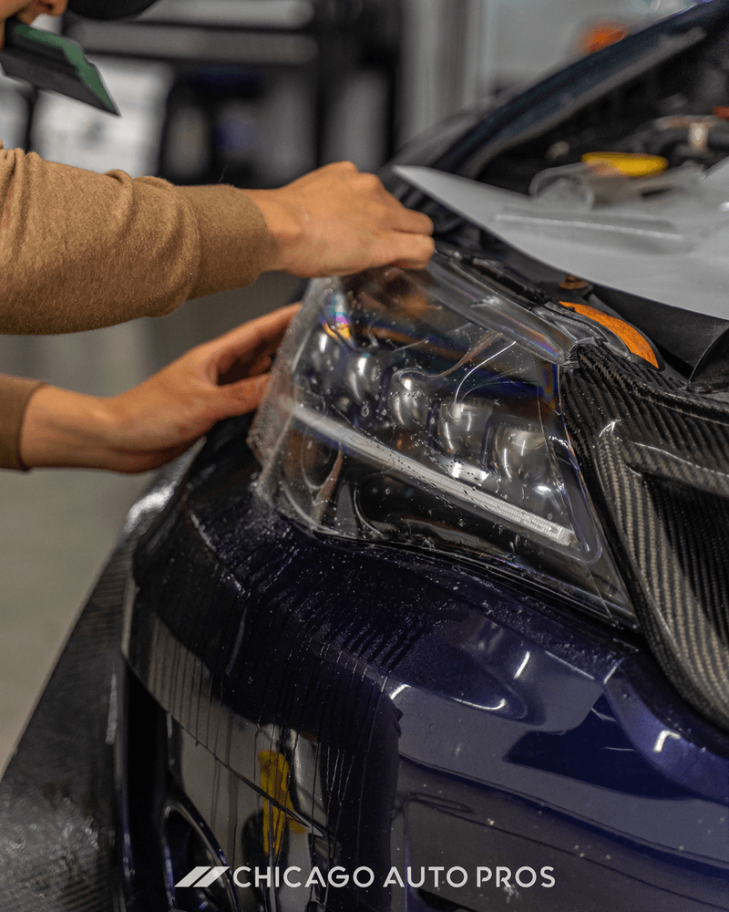 A person is putting a protective film on the headlight of a car.