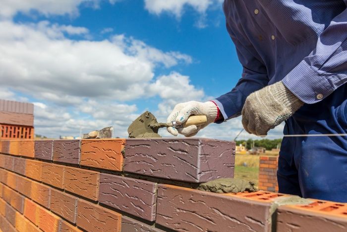 Bricklayer smoothing mortar on a brick wall under a blue sky