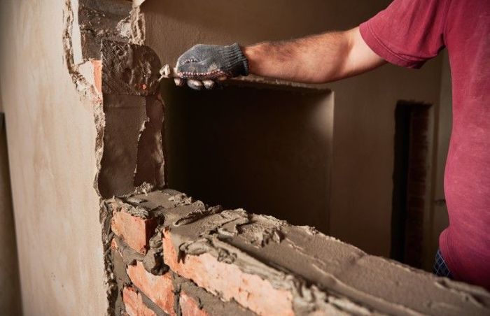 Worker using a chisel to break a brick wall indoors