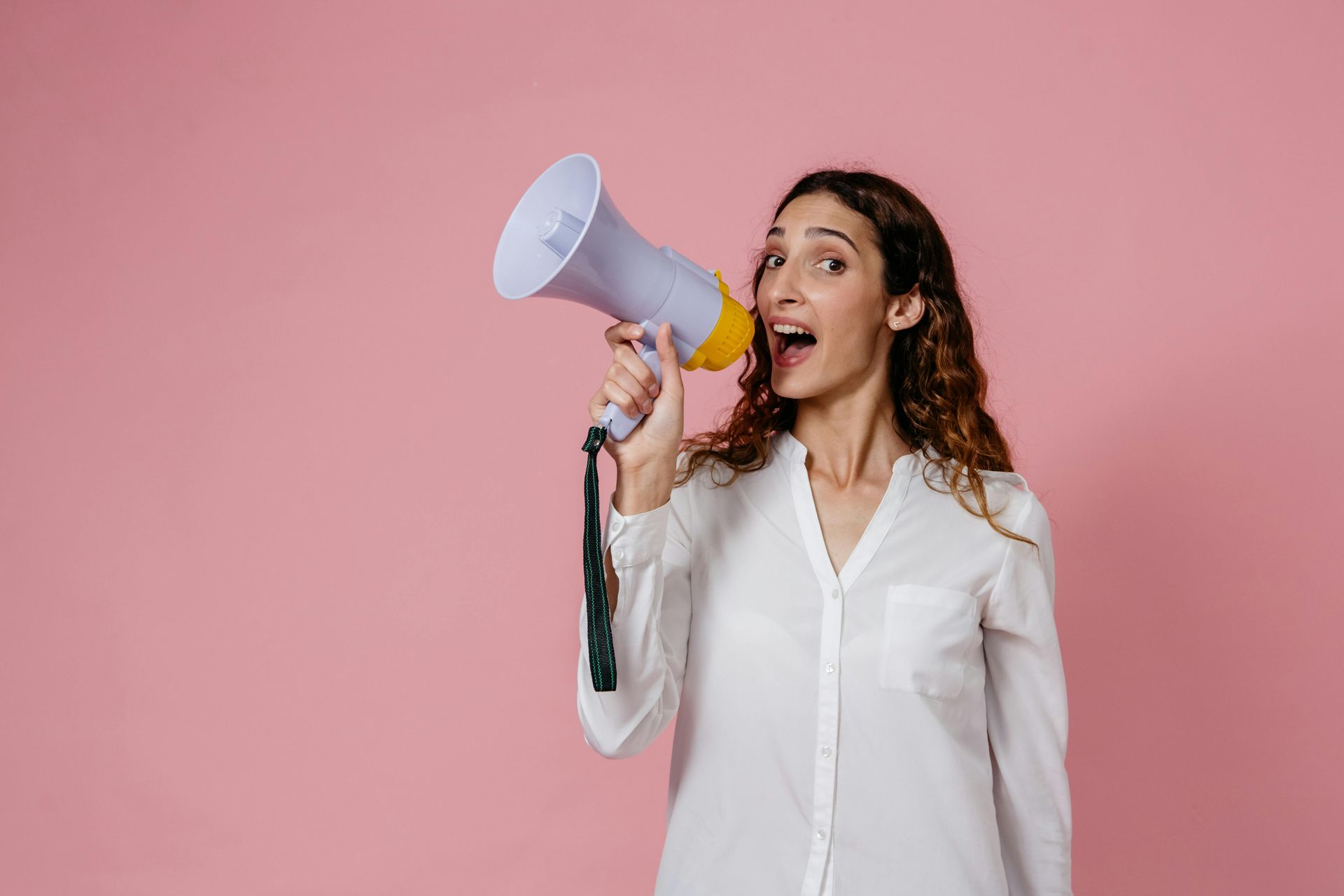 A lady in a white shirt with a pink background holding a mic to project her voice