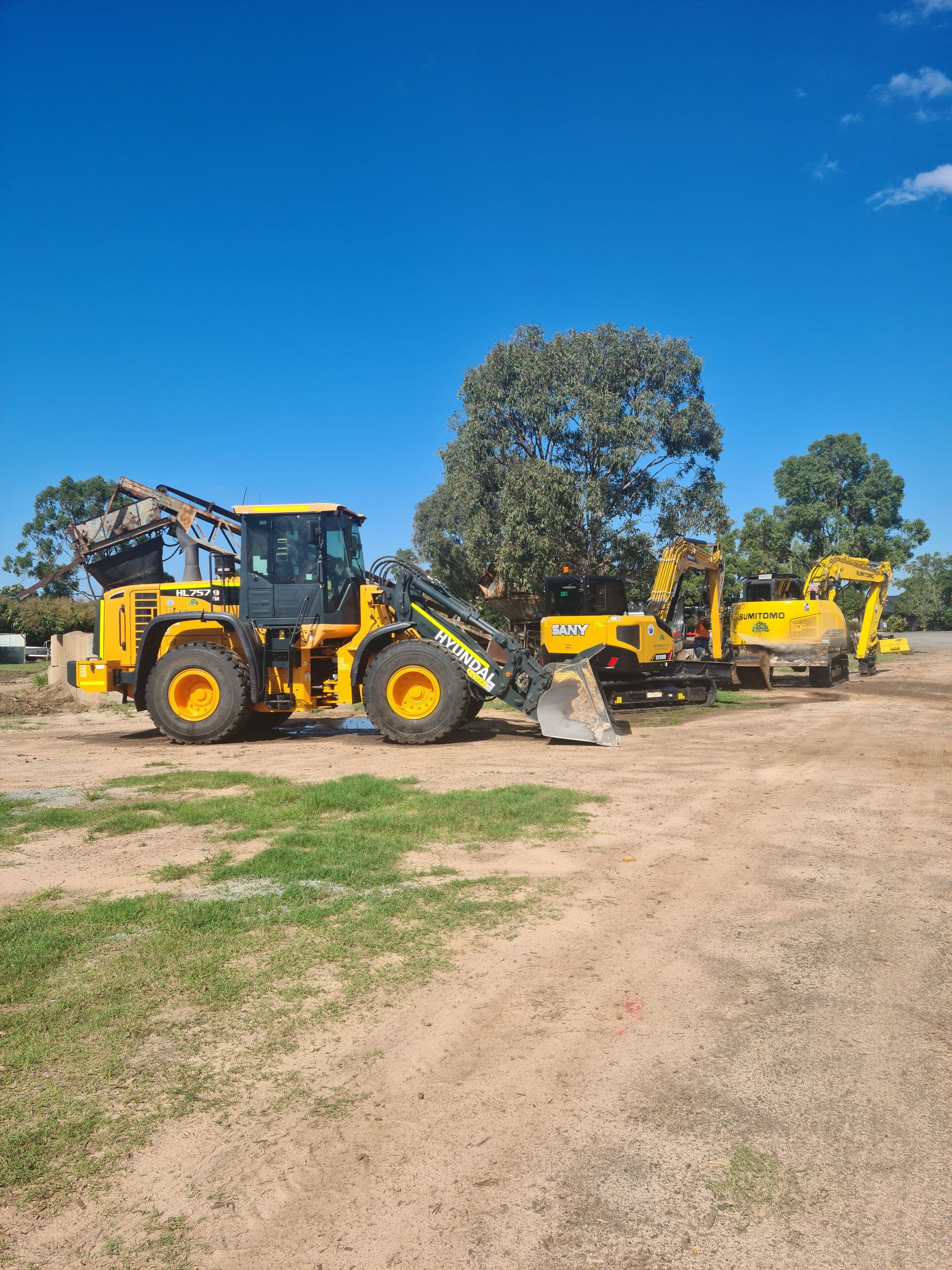A White Dump Truck is Towing an Excavator on a Trailer — A1 Tree Service in Childers, QLD