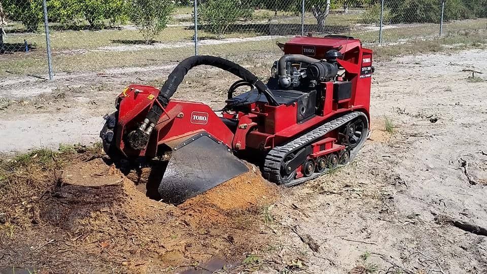 A Red Tractor is Cutting a tree Stump in the dirt — A1 Tree Service in Kensington, QLD