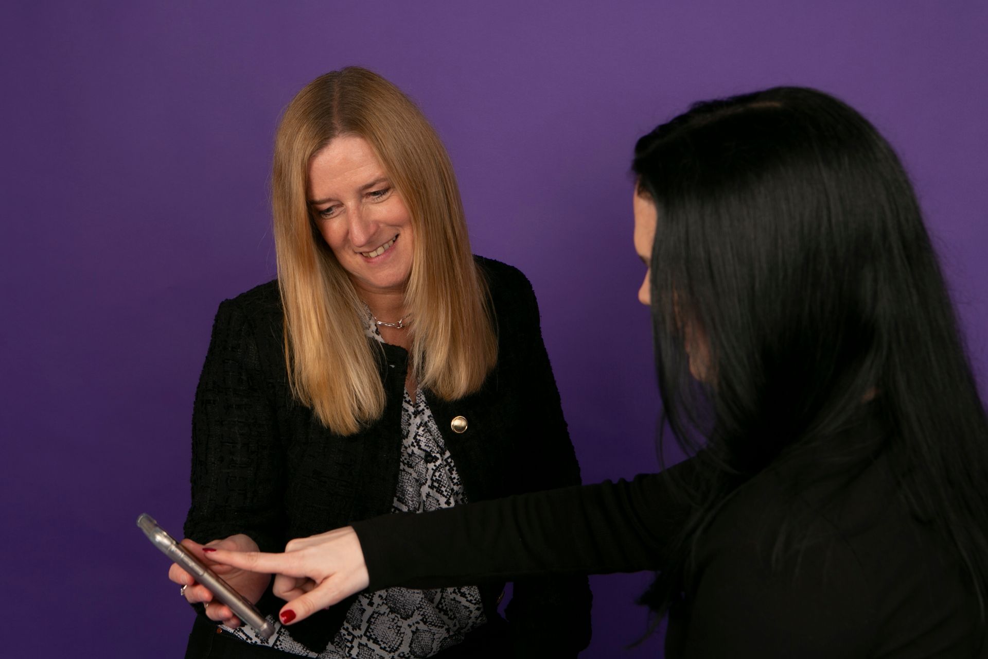 Two women are standing next to each other looking at a cell phone.