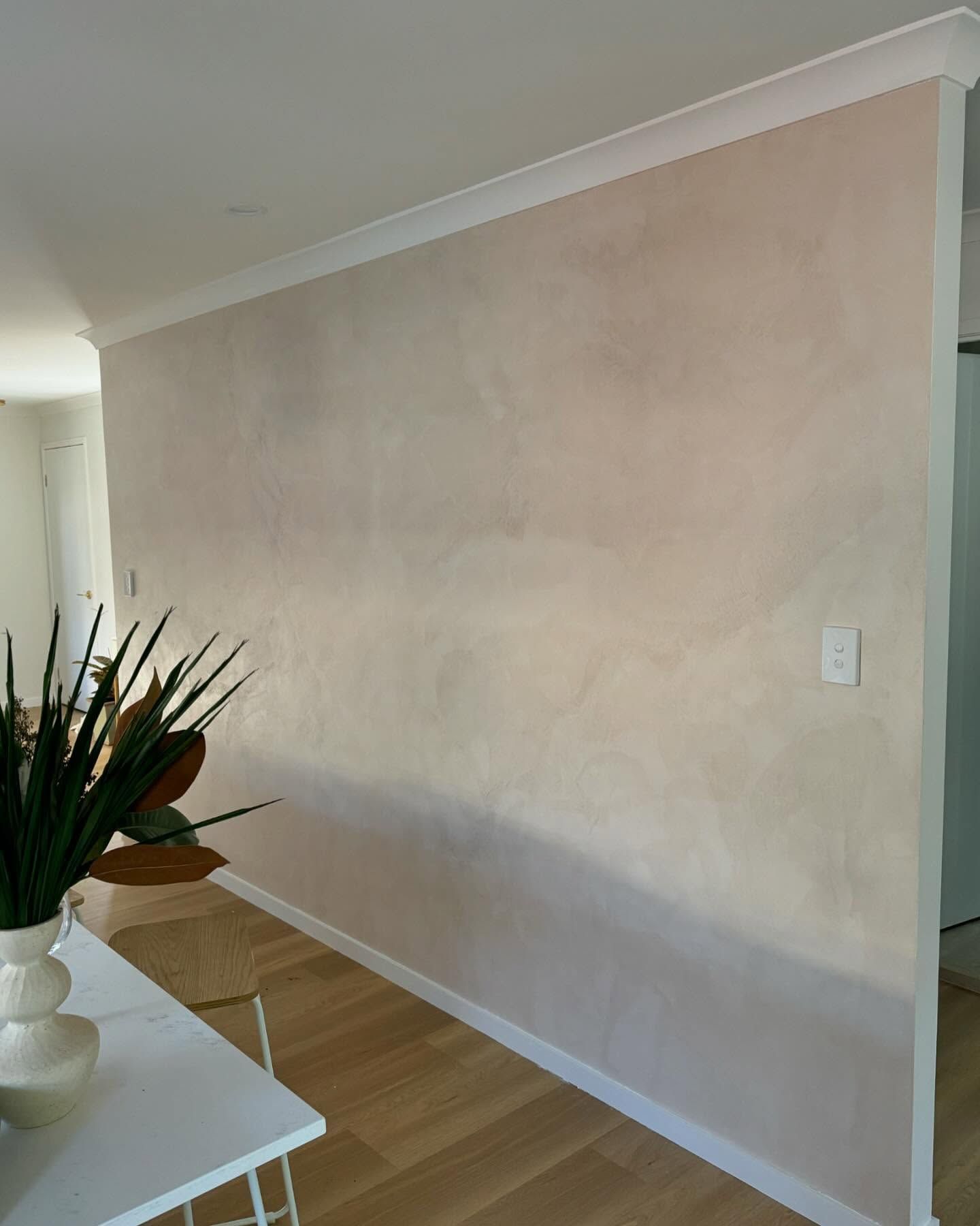 Empty beige hallway wall with white trim, wood floor, and a plant in the foreground
