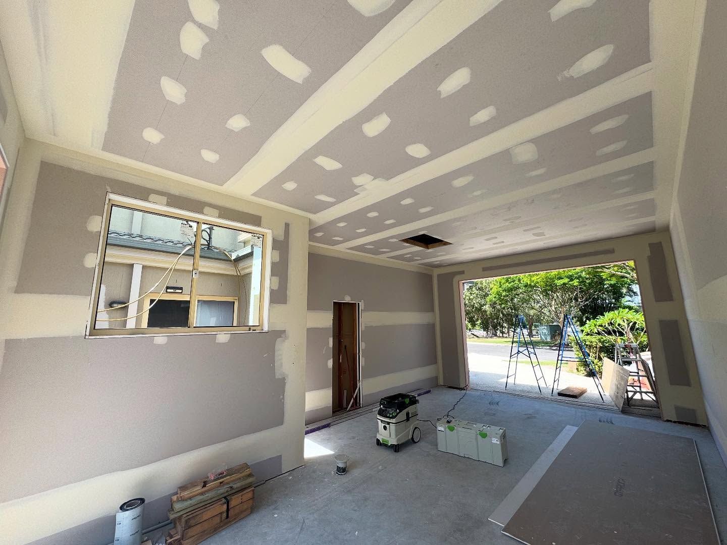 Unfinished garage interior with drywall patches, open door, window, and construction materials