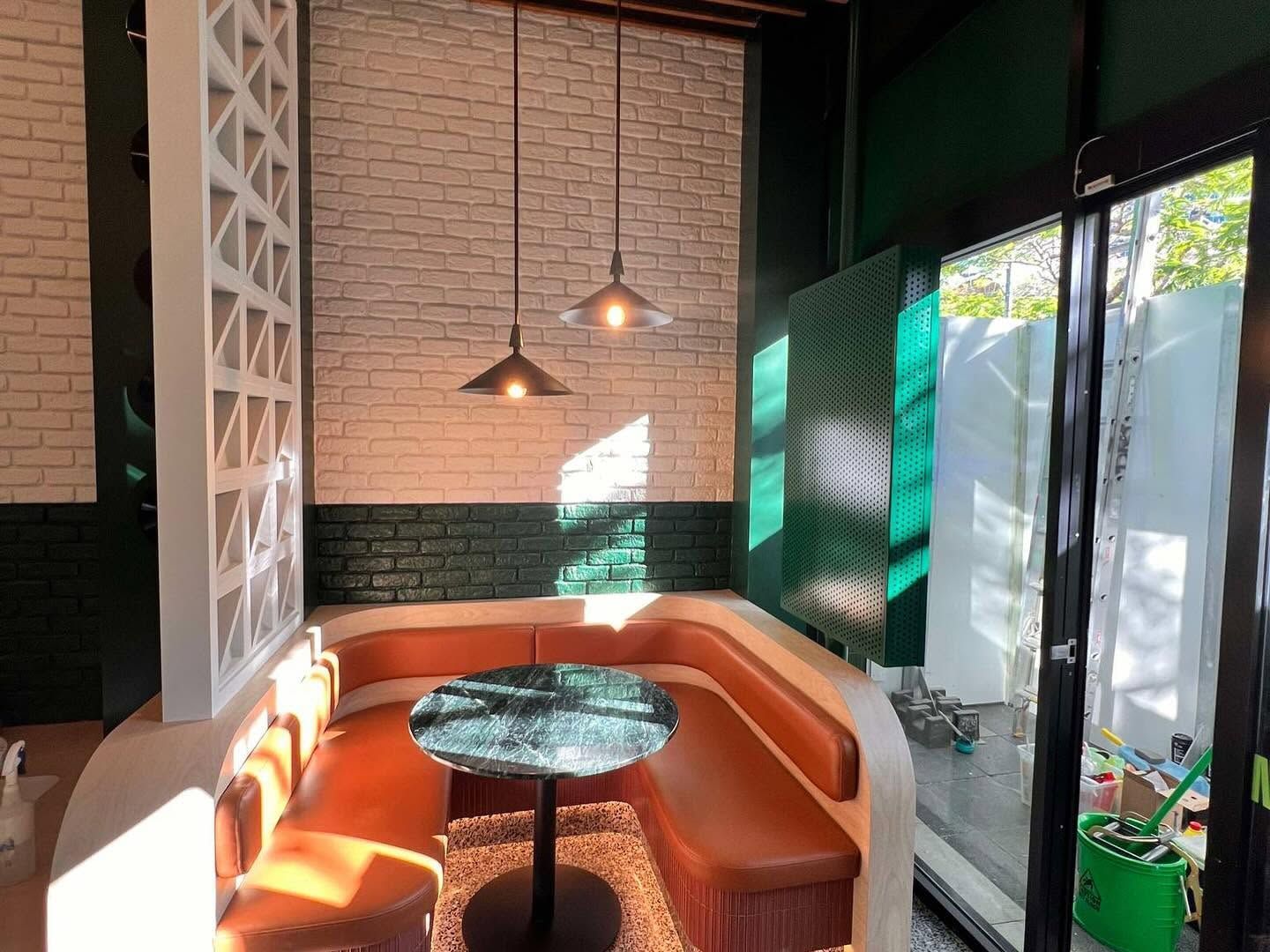 Cozy café booth with orange seating, a round table, hanging lights, and sunlight through large windows