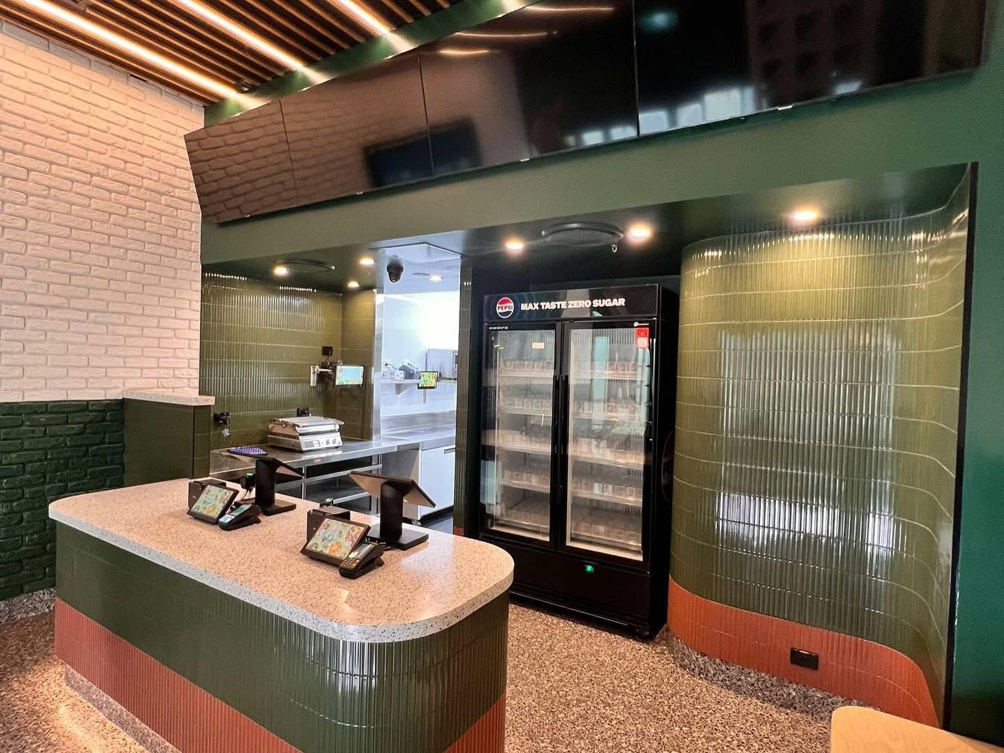 Restaurant entrance with a curved host counter, glass doors, and green-tiled walls under warm lighting