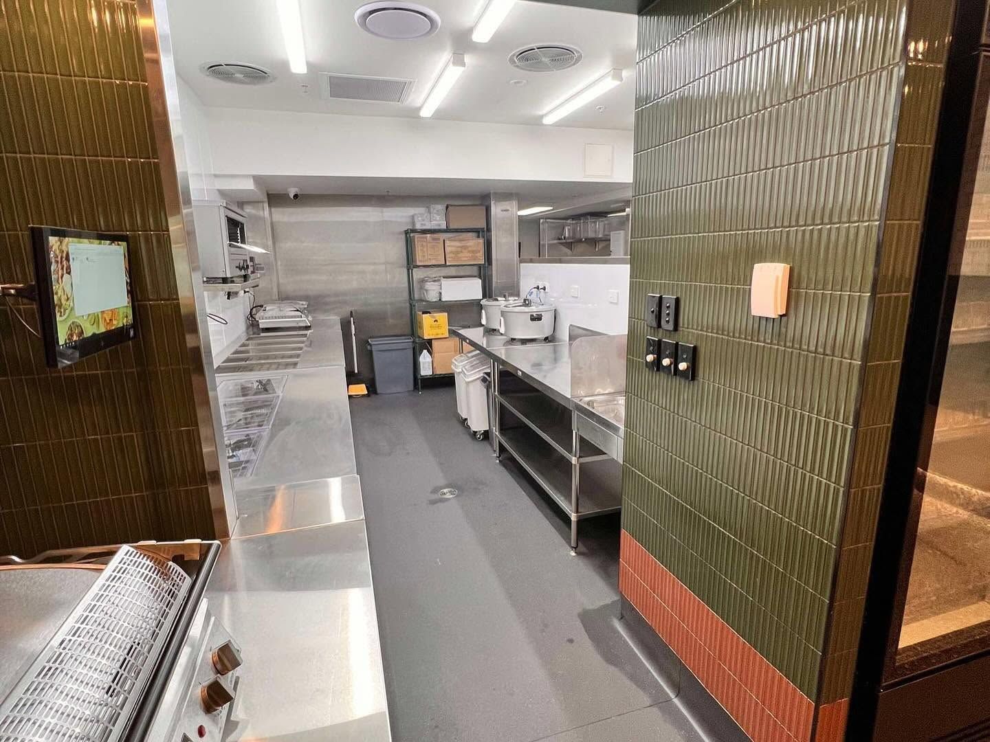 Commercial kitchen with stainless-steel counters, shelves, and equipment in a narrow corridor.