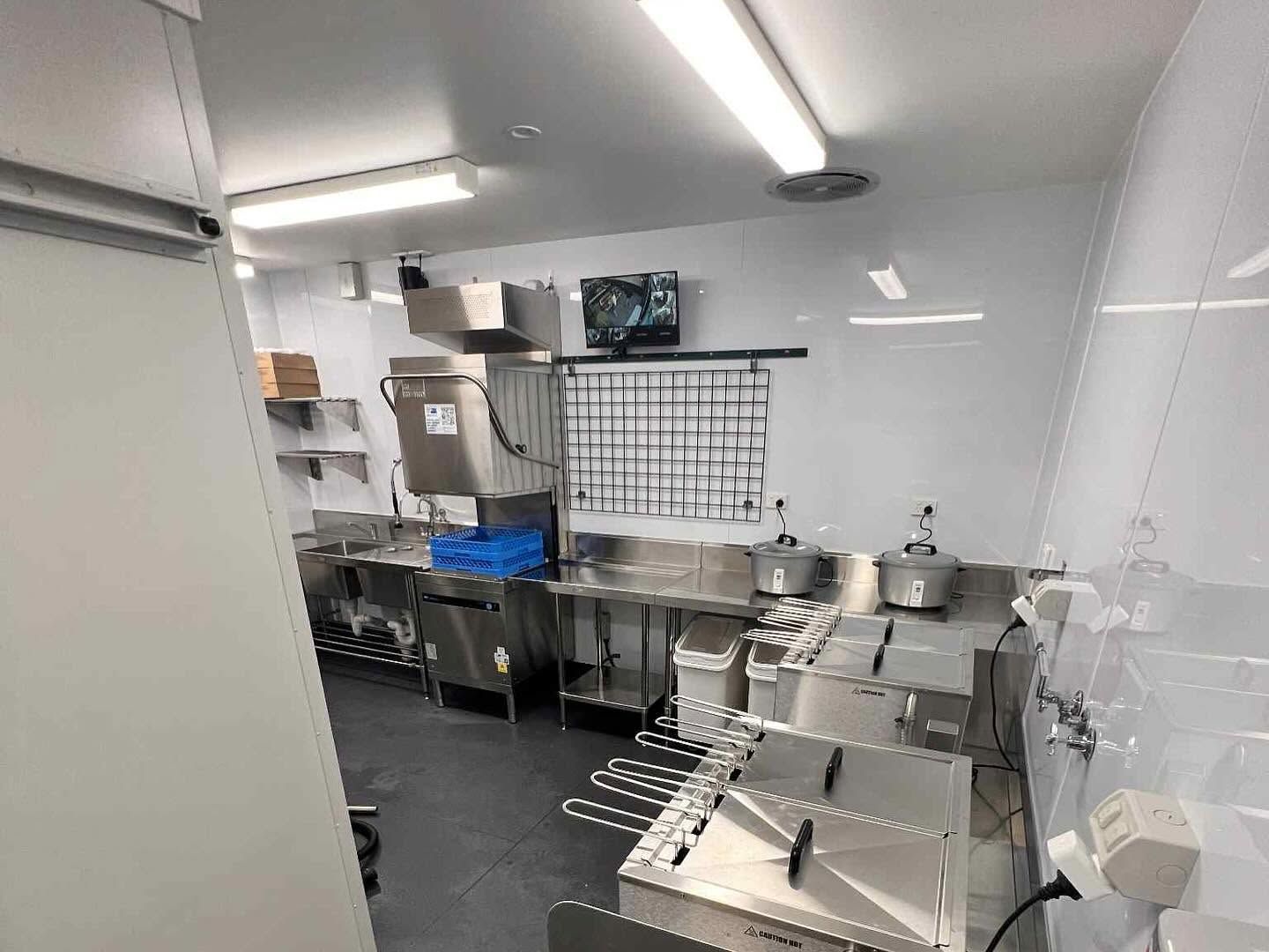 Clean stainless-steel commercial kitchen with sinks, prep tables, and storage racks.