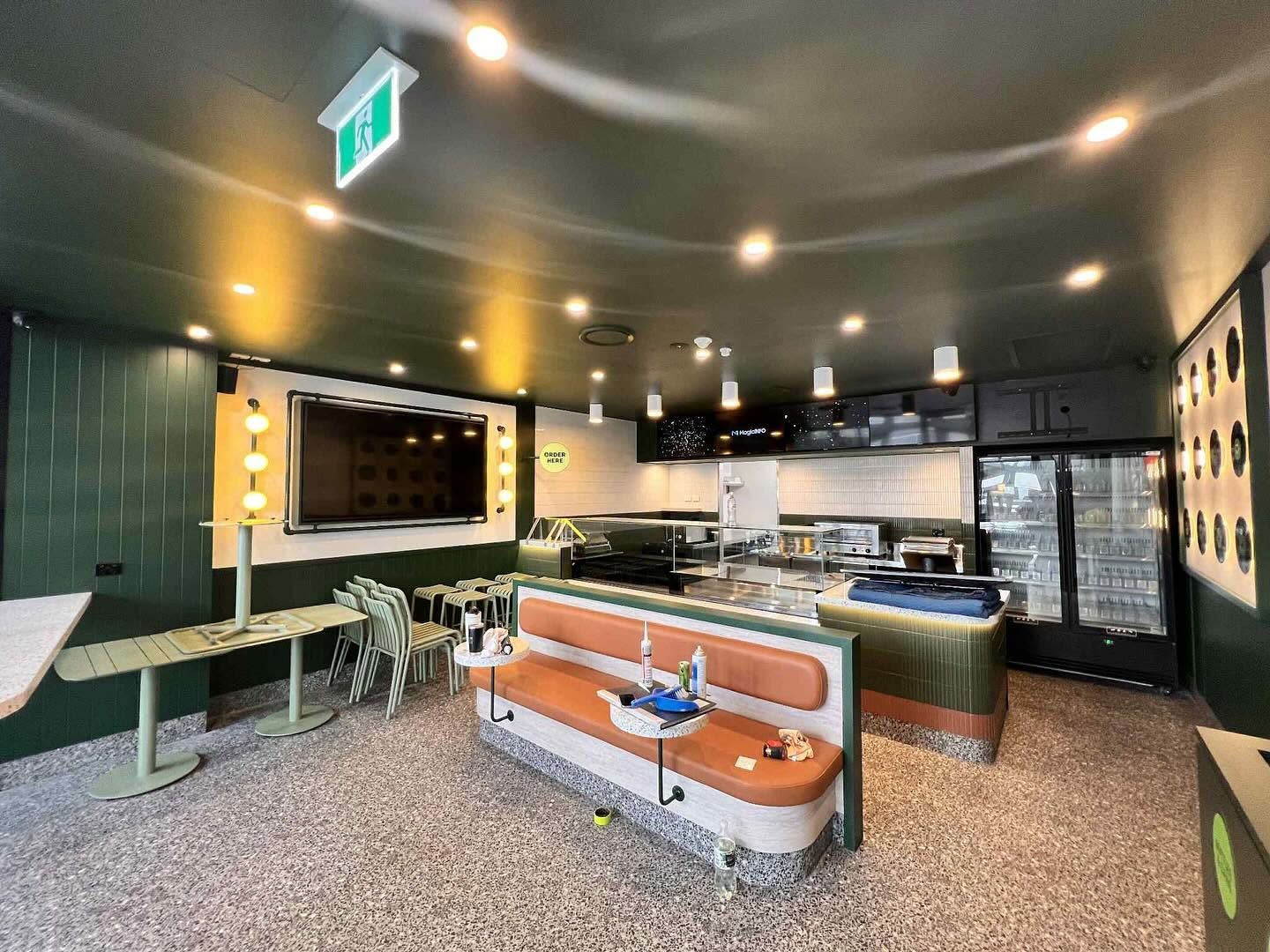 Stylish café interior with orange benches, green tables, a bar counter, and warm ceiling lights