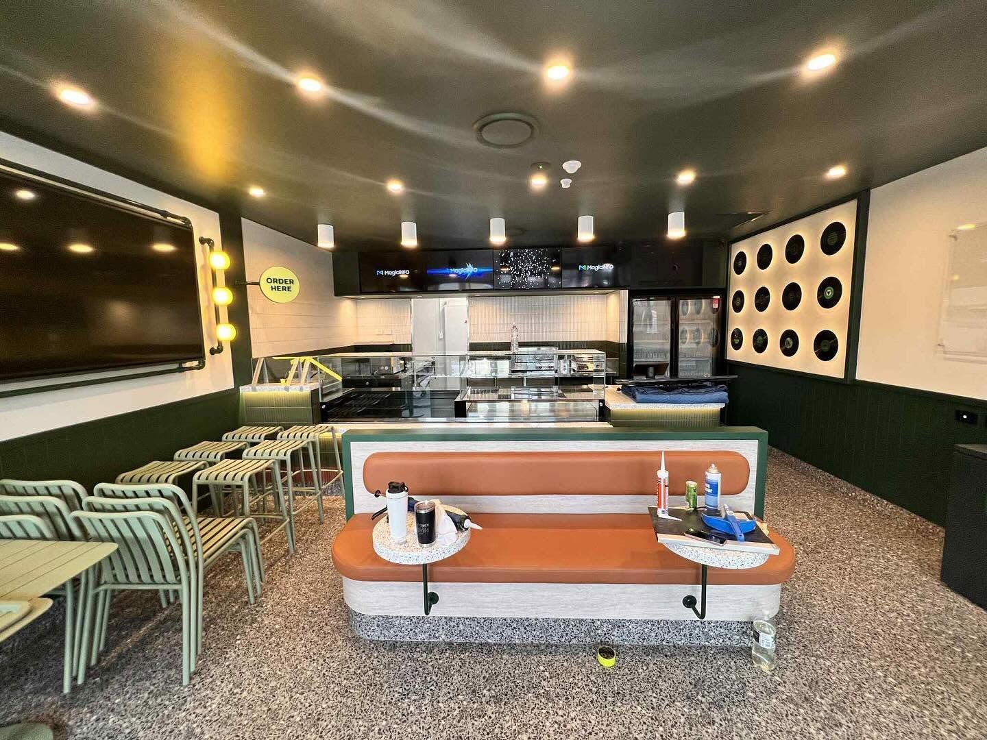 Modern cafe interior with orange seating, mint chairs, a long counter, and warm ceiling lights