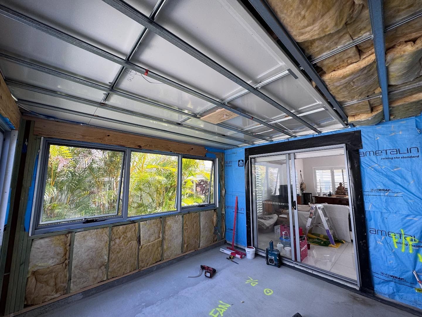 Unfinished room with blue insulation, exposed walls, and sliding glass doors to a patio.