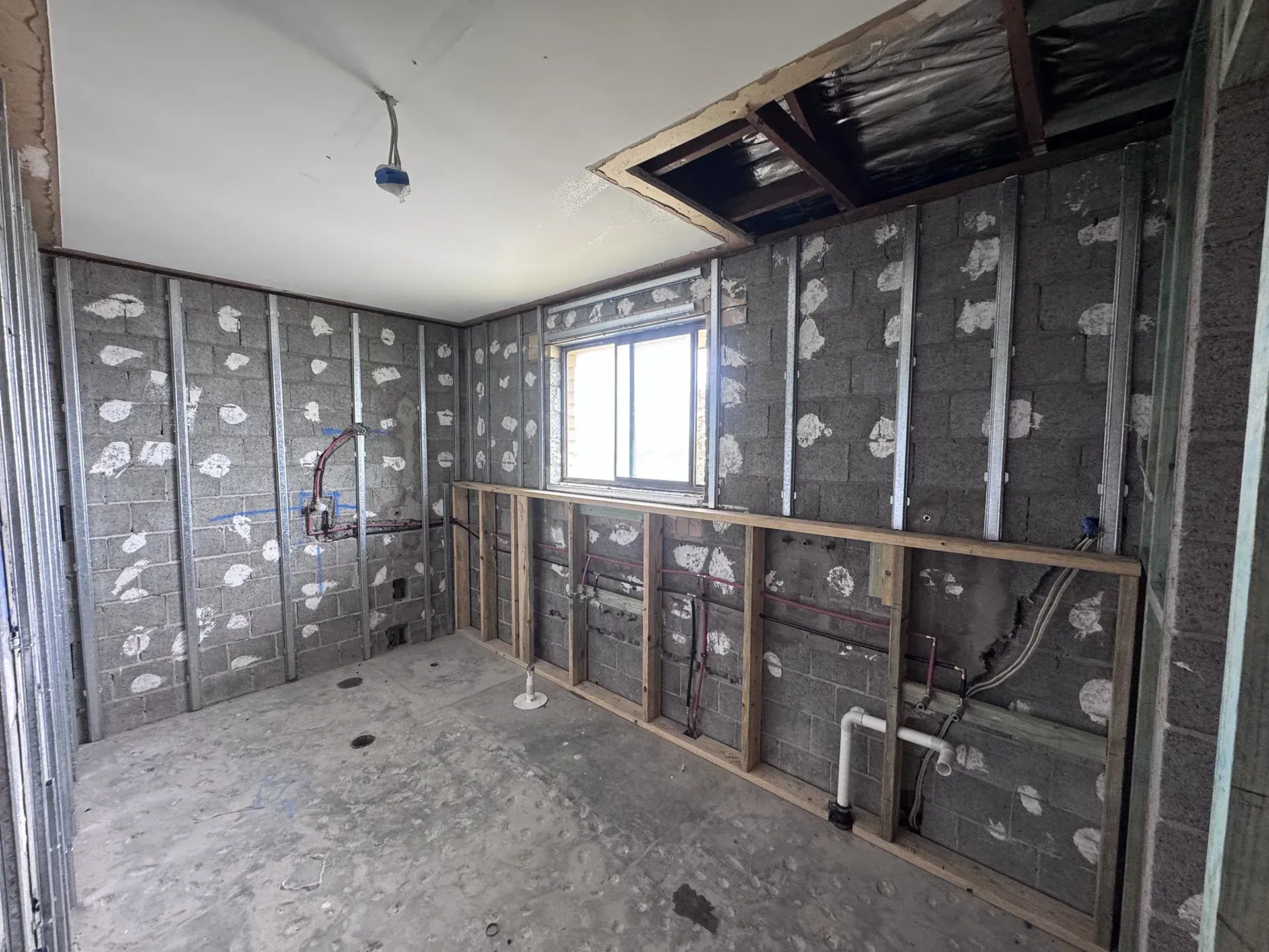 Interior of an unfinished room with exposed insulation, drywall studs, a window, and construction debris on the floor