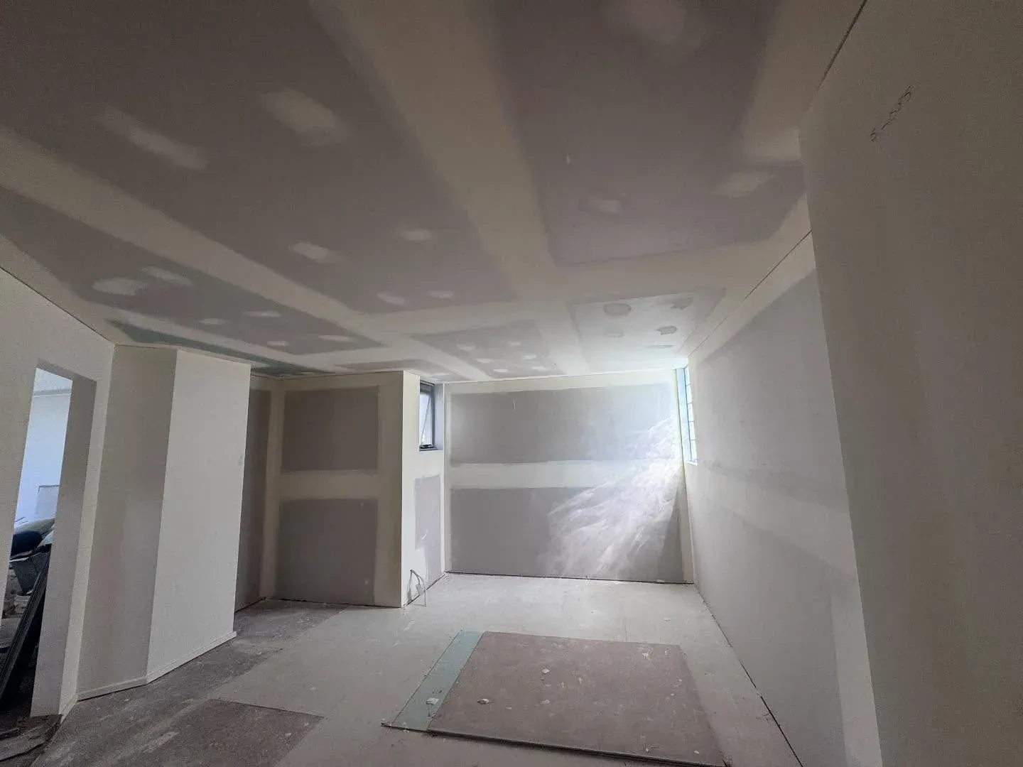 Unfinished room with drywall, recessed lights, and a bright window at the far end.
