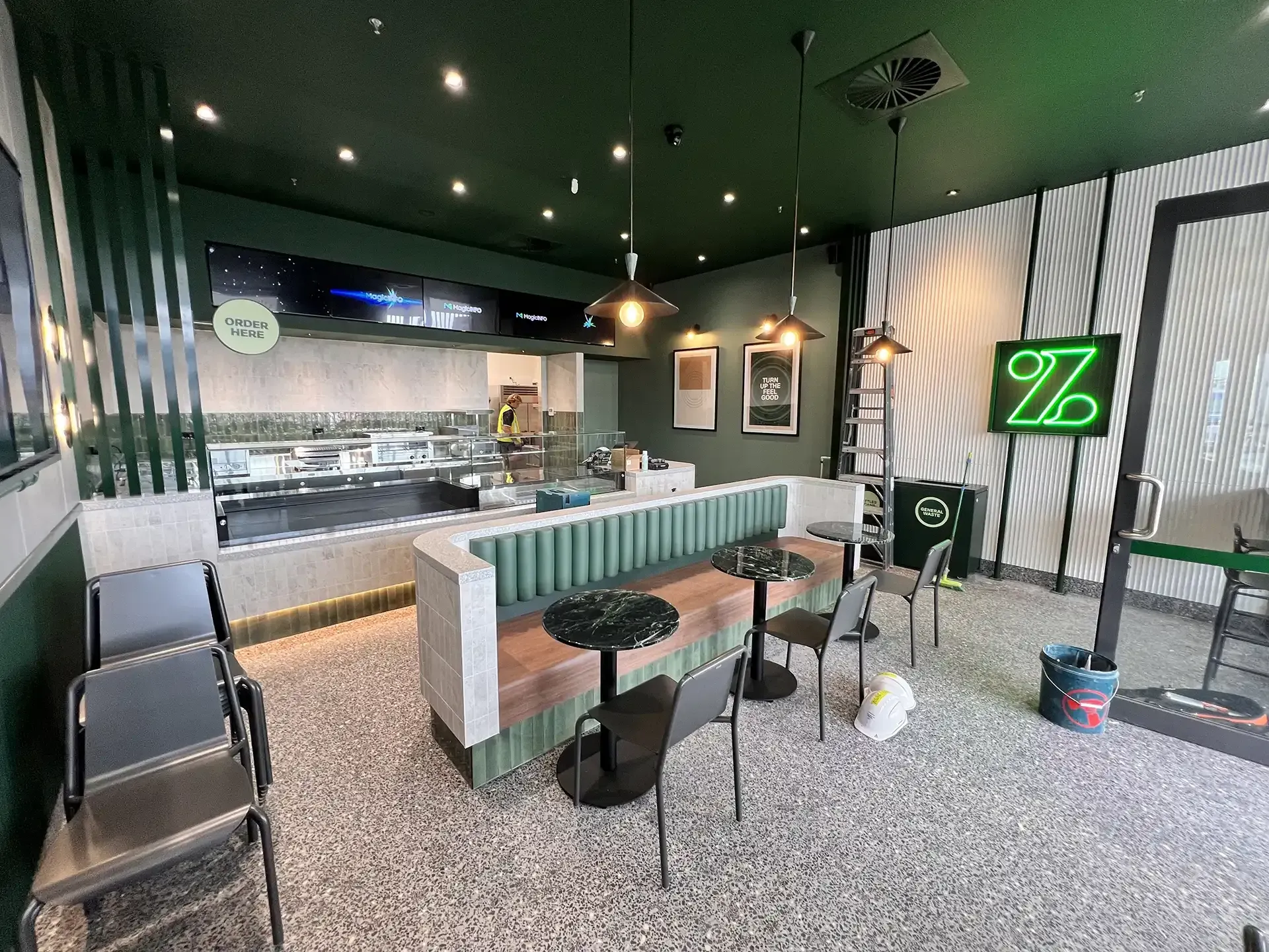 Stylish cafe interior with green accents, counter seating, hanging lights, and black chairs on speckled flooring