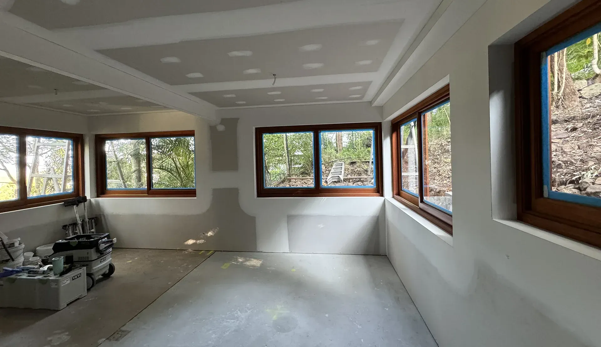 Empty unfinished room with white drywall, exposed floor, and large windows letting in daylight