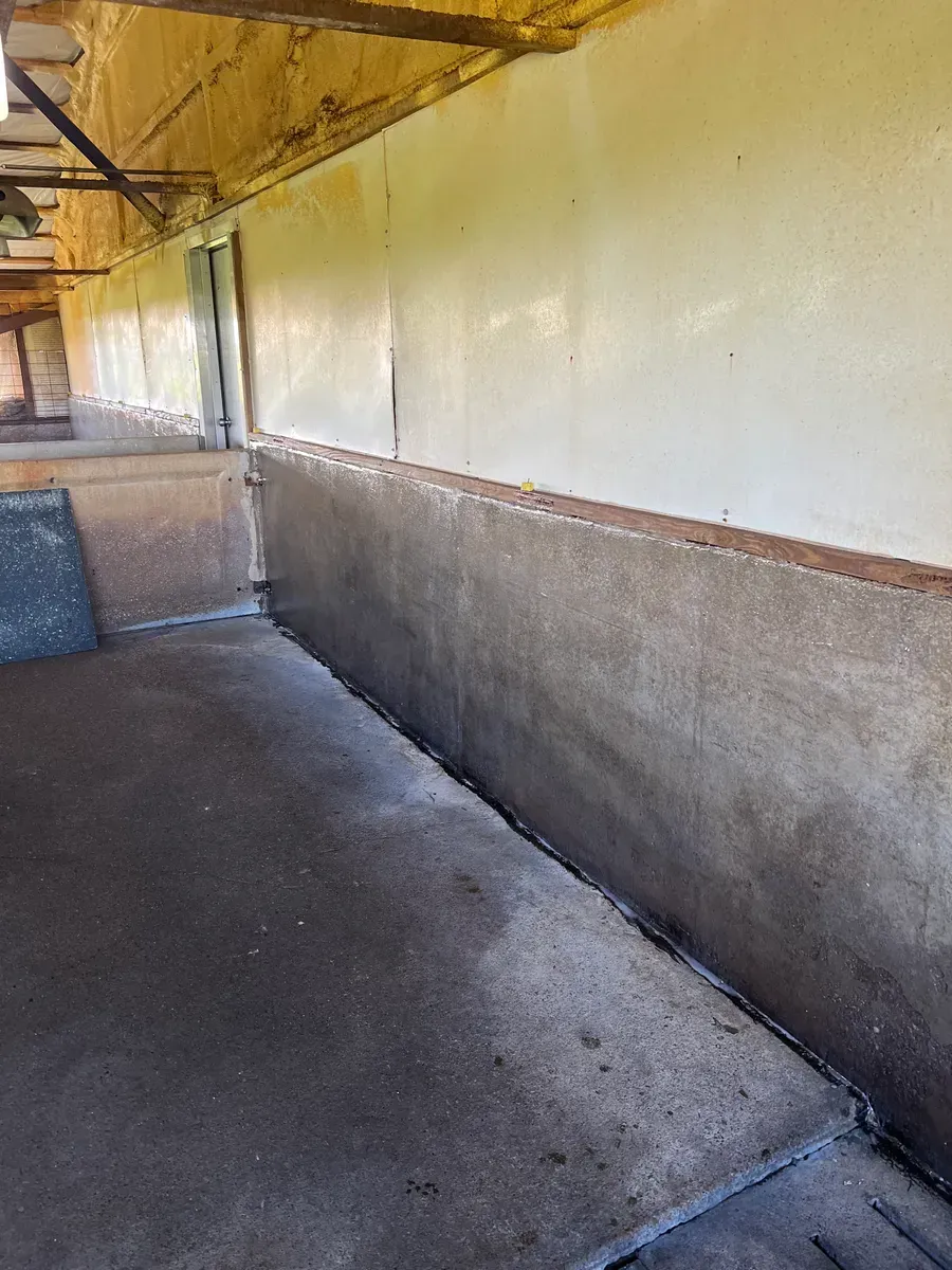 A long hallway with a concrete floor and a white wall.