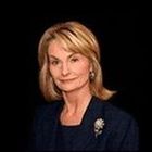 A woman wearing a blue jacket and a brooch is smiling for the camera.