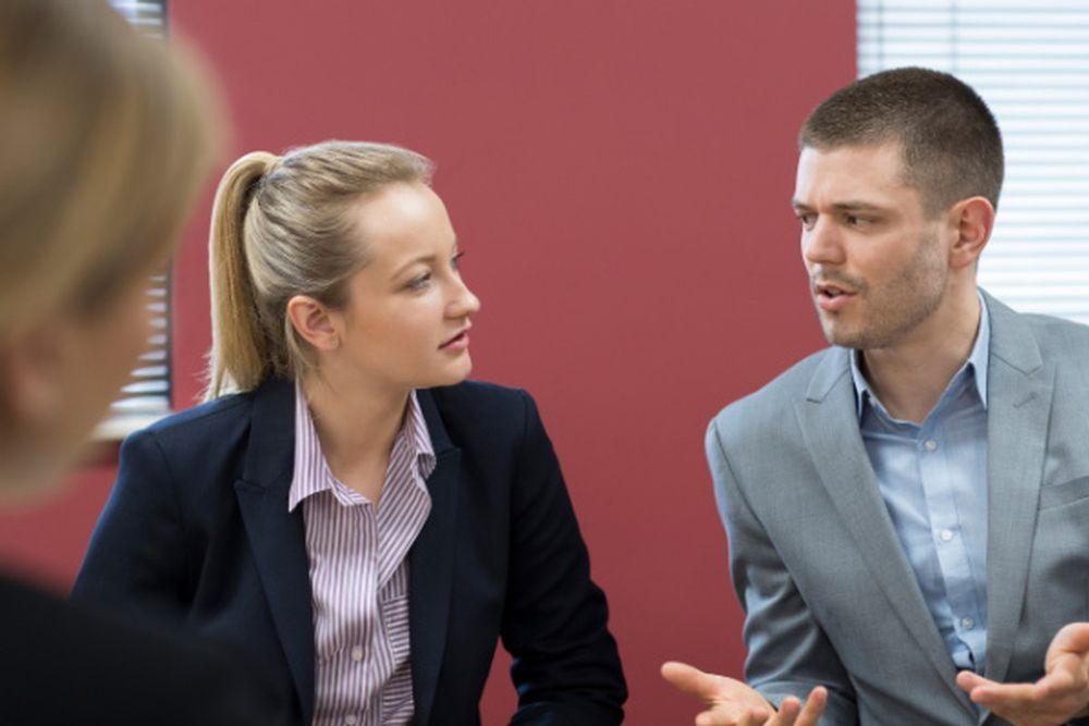 A man and a woman are sitting at a table talking to each other.