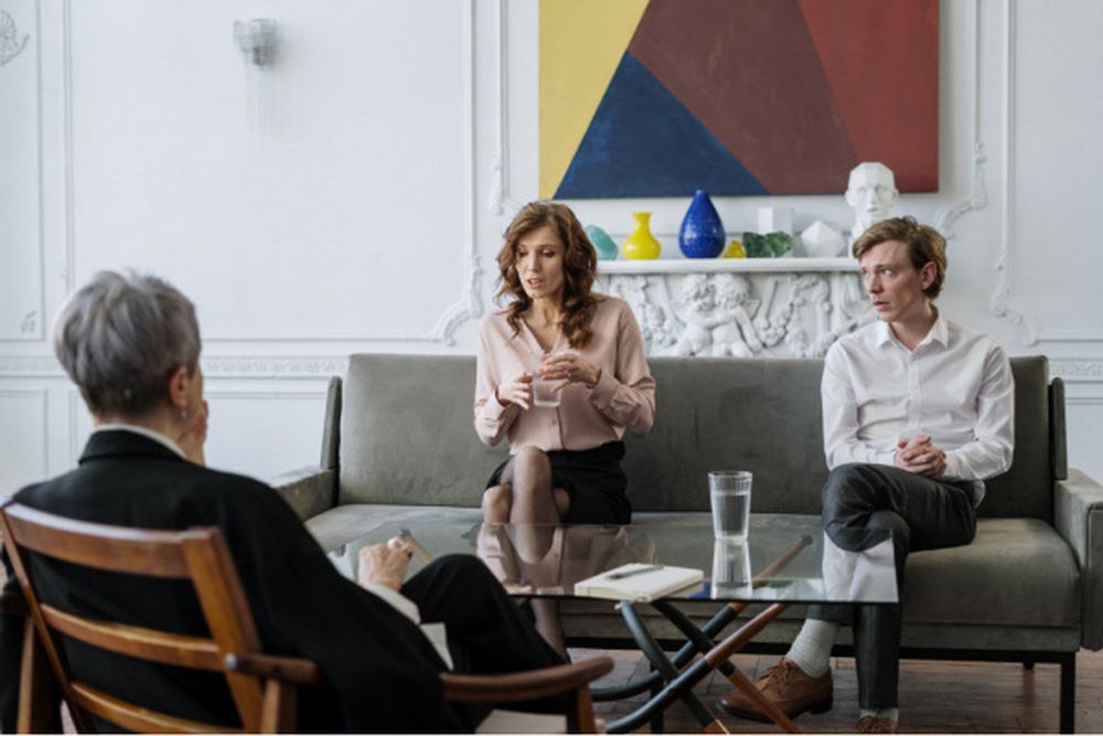 A man and a woman are sitting on a couch talking to a woman.