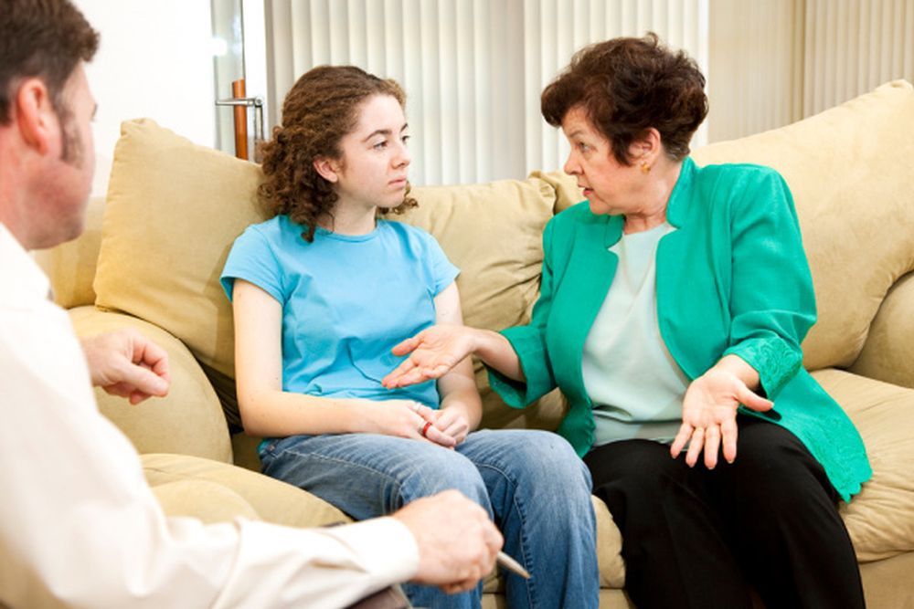 A man and two women are sitting on a couch talking to each other.