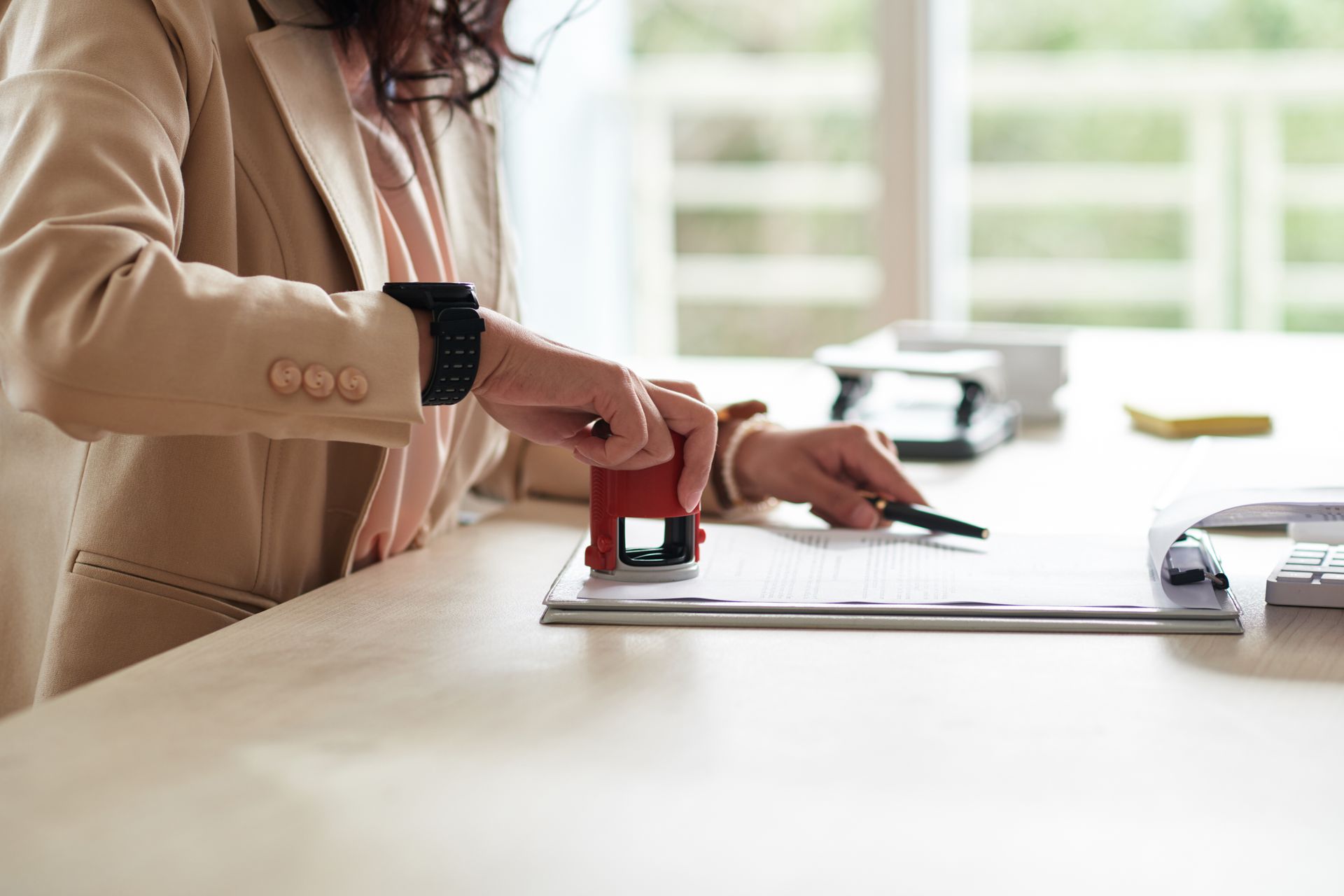 A woman is sitting at a desk using a stamp on a piece of paper.