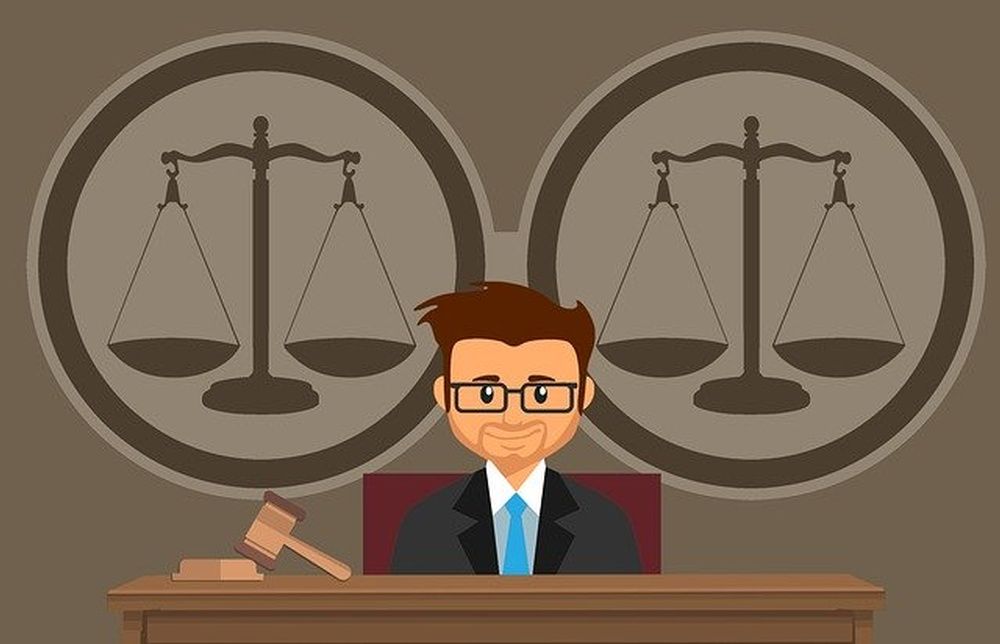 A judge is sitting at a table with a gavel and scales of justice in the background.