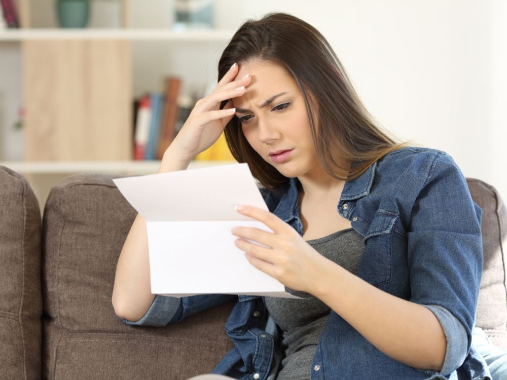 A woman is sitting on a couch reading a letter.