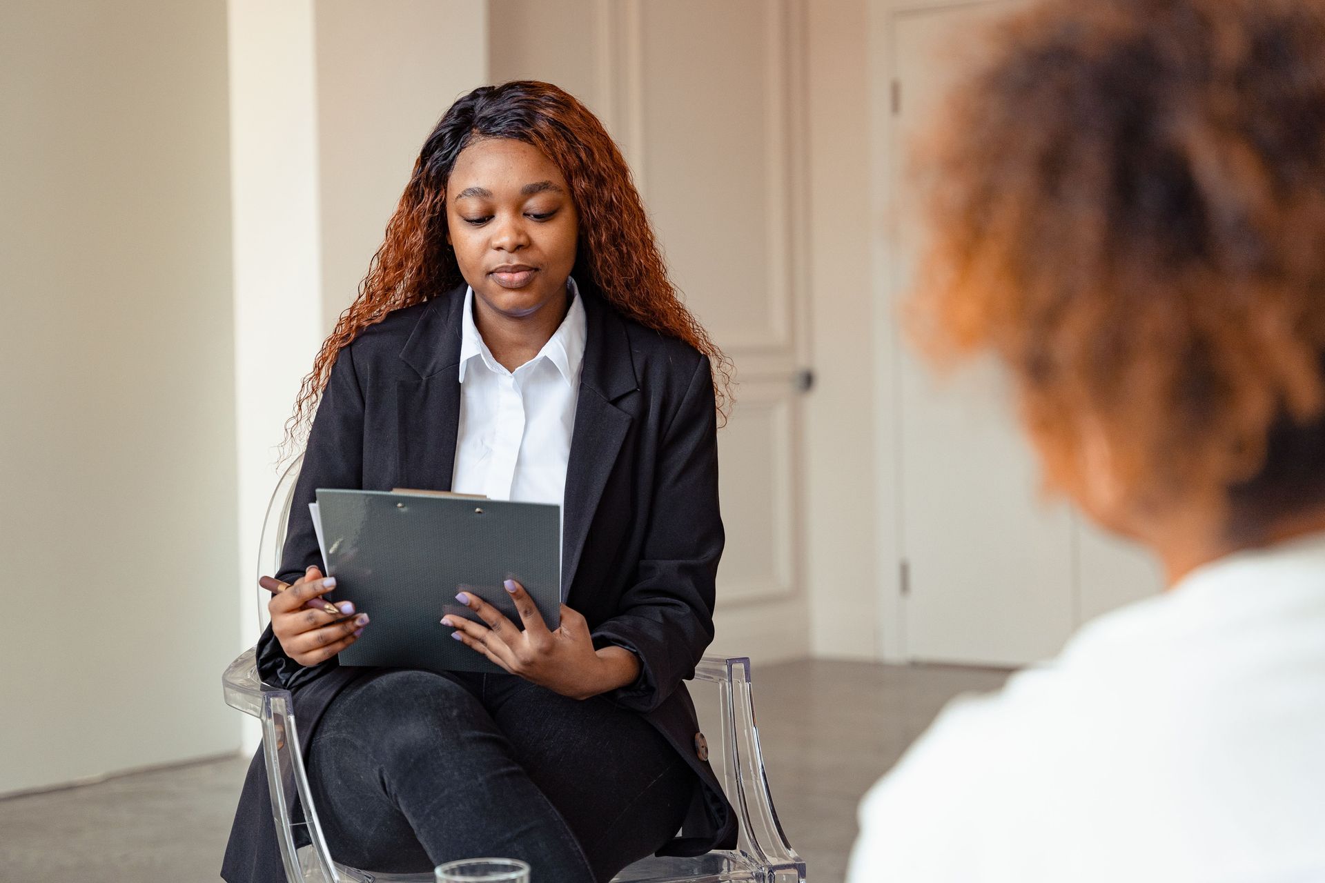 Woman in a black blazer holding a tablet during a seated interview in a bright office.