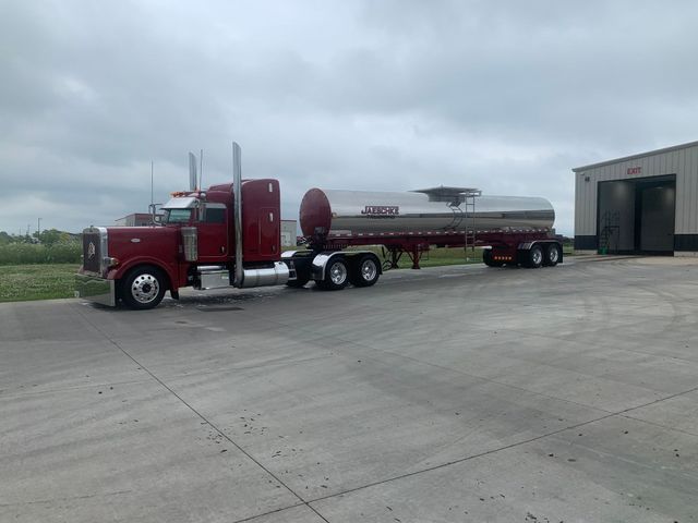 A red semi truck is parked in a parking lot next to a building.