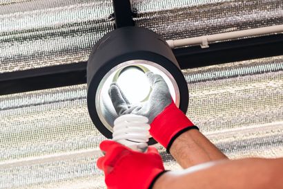 Gloved hand installing a light bulb into a ceiling fixture under a mesh shade