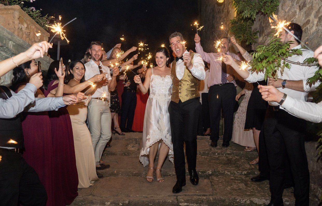 Wedding couple walking through a sparkler send-off surrounded by guests outdoors at night
