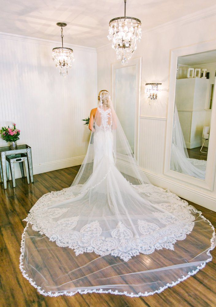 Bride in white gown with long veil and lace train in a bright room with chandeliers