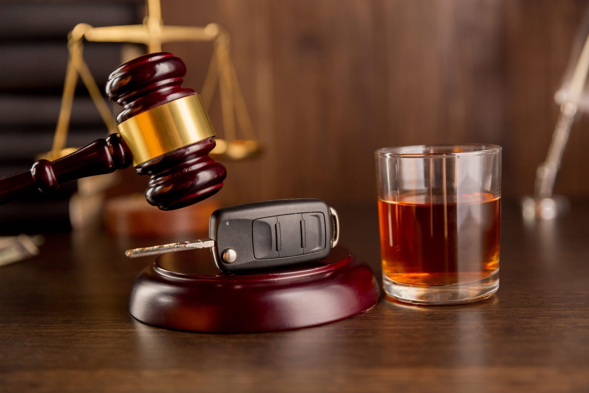 Gavel beside car key and glass of whiskey on a courtroom desk
