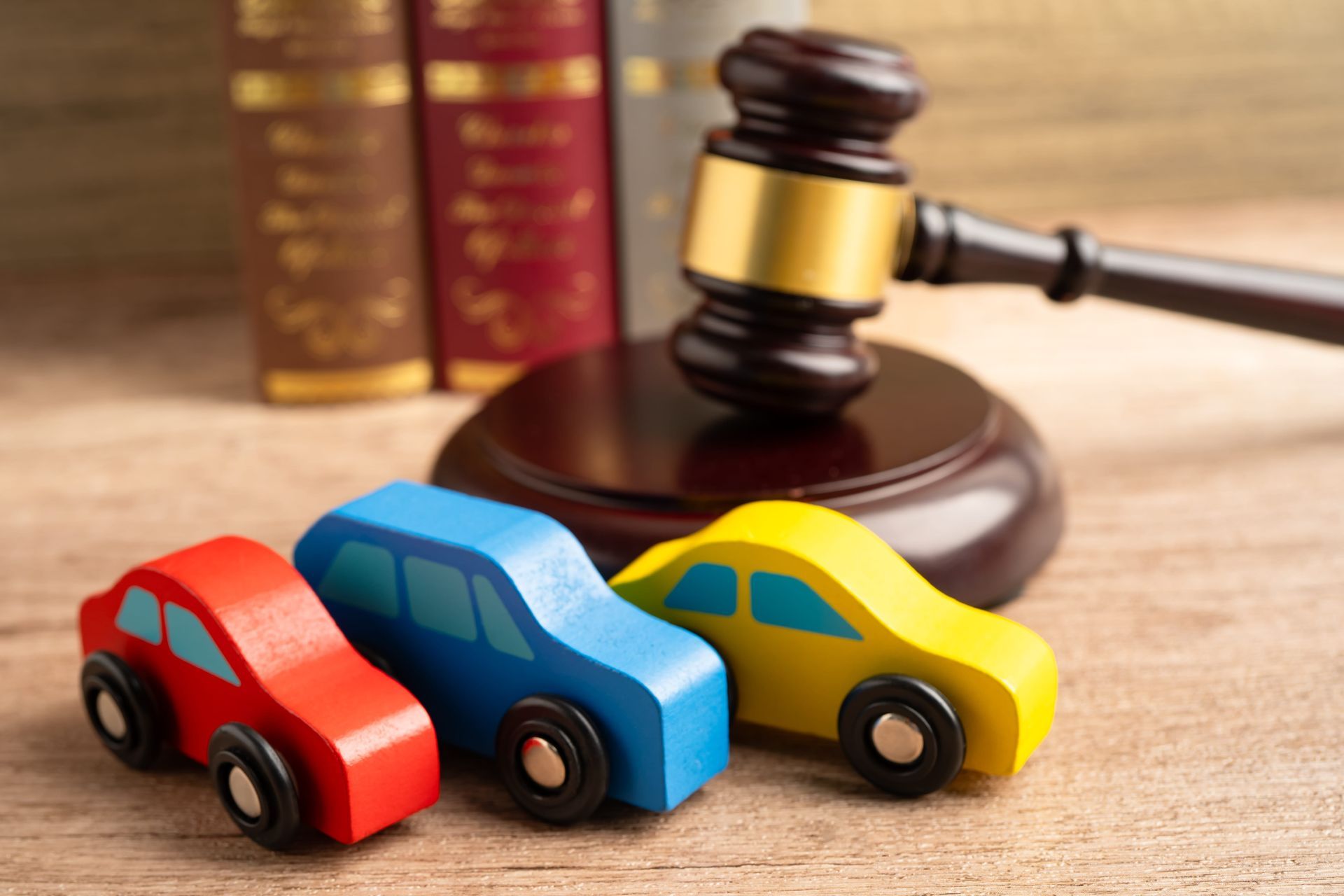 Toy cars beside a judge’s gavel on a wooden table, suggesting a courtroom or legal theme