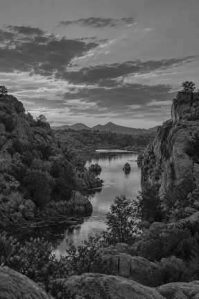 Black-and-white river valley with cliffs, dense trees, and a distant boat under cloudy skies